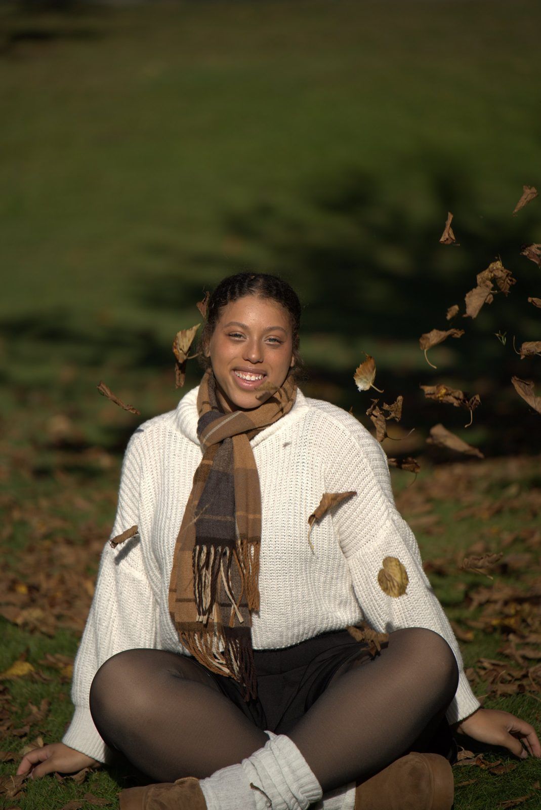 Smiling portrait sitting cross-legged as autumn leaves fall